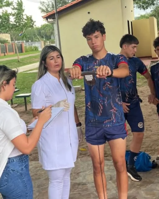 La licenciada Lilian Sosa, de guardapolvo blanco, midiendo la composición corporal de un jugador de un plantel juvenil mientras una asistente anota